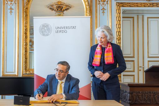 Zu sehen ist sitzend und ins Goldene Buch der Uni Leipzig schreibend der Botschafter Indiens in Deutschland, Ajit Vinayak Gupte. Neben ihm steht Rektorin Prof. Dr. Eva Inés Obergfell. Foto: Swen Reichhold